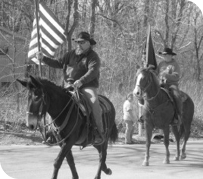 black and white photo of two people riding horses with flags in hand, one the american flag and one that can't be made out.