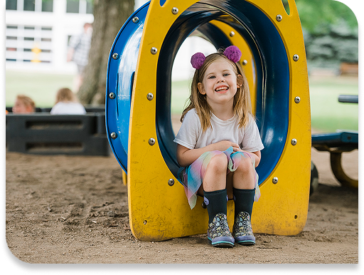 young girl smiling sitting inside of a colorful yellow and blue tube in a park